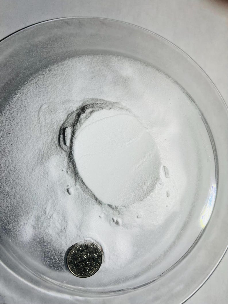 May include: A white powder in a clear glass bowl with a US quarter coin for scale.