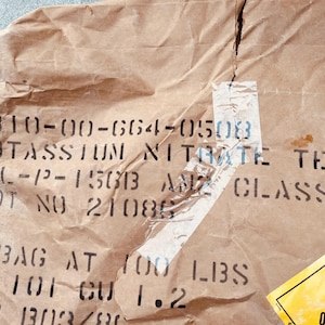 May include: A brown paper bag with black printed text that reads "6810-00-664-0503 POTASSIUM NITRATE TECH -12-15013 ANZ CLASS2 LOT NO 21086 1 BAG AT 100 LBS NT 101 CU 1.2 001303/80". A yellow and black warning label with the word "OXIDIZED" is visible on the right side of the bag.