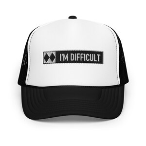 Peut inclure: Un chapeau de camionneur blanc et noir avec un patch noir qui dit "I'M DIFFICULT" et un symbole de diamant noir.