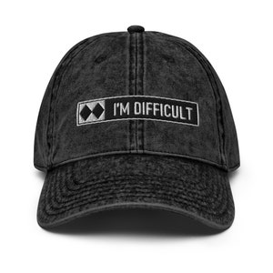Könnte beinhalten: Schwarze, abgenutzte Baseballkappe aus Denim mit einem weißen gestickten Aufnäher, auf dem "I'M DIFFICULT" und ein schwarzes Diamantsymbol stehen.