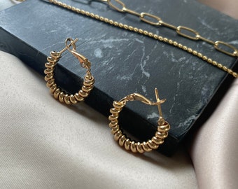 May include: Two gold hoop earrings with a coiled design. The earrings are on a black marble surface.