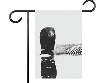 May include: A black and white photograph of a loon swimming in the water. The loon's head is above the water, and its body is submerged. The water is calm and reflects the loon's image.