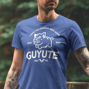 Puede incluir: Una camiseta azul con un gráfico blanco de un cerdo y el texto "Espero que esto vuelva a suceder 1973 GUYUTE 1994 Ugly Pig".