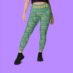 Puede incluir: Leggings verdes con un patrón de cerdos amarillos y la palabra "GUYUTE" impresa en la cintura.