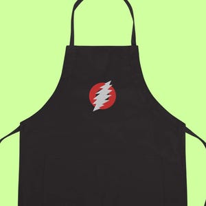 May include: Black apron with a red circle and a white lightning bolt design. The apron has a neck loop and waist ties. The apron is made of a durable fabric and is suitable for cooking or crafting.
