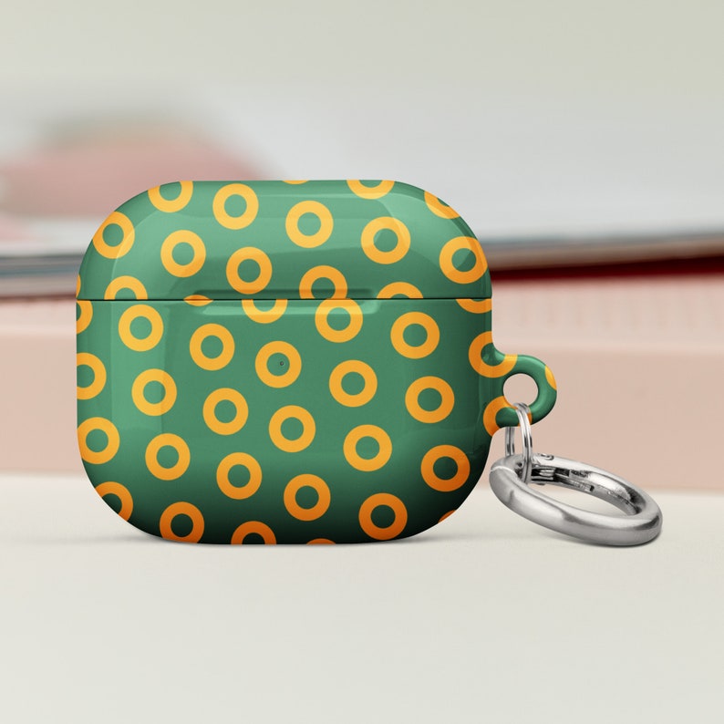 Peut inclure: &Eacute;tui vert pour Airpods avec un motif de cercles orange. L'&eacute;tui est dot&eacute; d'un porte-cl&eacute;s en m&eacute;tal argent&eacute;.