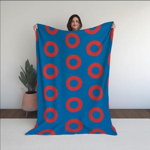 May include: A blue fleece blanket with a repeating pattern of red donuts. The blanket is being held up by a person.