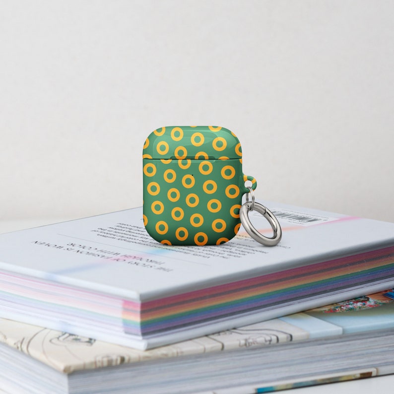 Peut inclure: Une coque pour Airpods verte et jaune avec un motif de beignets et un porte-cl&eacute;s argent&eacute;.