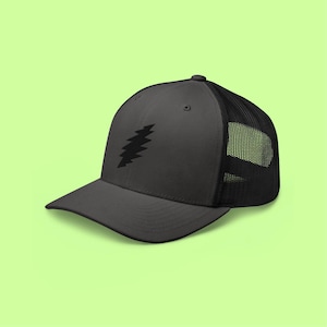 May include: A black trucker hat with a black zig-zag design on the front. The hat has a curved brim and a mesh back. The hat is set against a light green background.