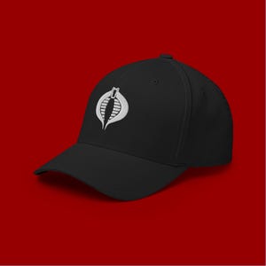 May include: A black baseball cap with a white embroidered Cobra logo. The logo is a stylized cobra with a raised hood.
