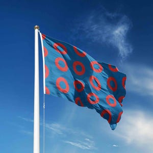 May include: A blue flag with a pattern of red circles blowing in the wind against a bright blue sky. The flag is mounted on a white flagpole with a gold finial.
