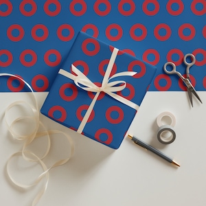May include: A blue and red gift wrap with a donut pattern. A white ribbon is tied around a gift box wrapped in the paper. The gift box is sitting on a white surface.