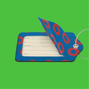 May include: Blue luggage tag with red donut pattern. The tag has a flap that folds over to reveal a blank space for writing name, tel, address, and e-mail.