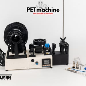 K&ouml;nnte beinhalten: Eine vormontierte PETmachine von Tylman Design mit wei&szlig;er Basis, gro&szlig;em schwarzen Zahnrad, digitalem Temperaturregler und verschiedenen mechanischen Komponenten. Enthalten sind Metalld&uuml;sen, blaue und silberne Dr&auml;hte sowie eine Zange.