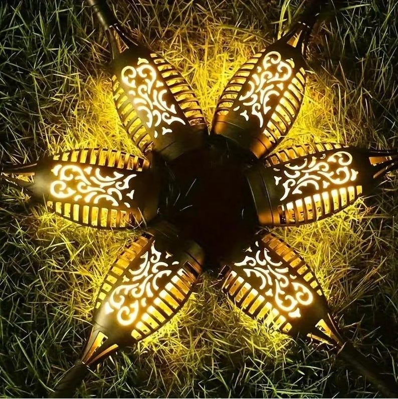 May include: Six solar powered flame lights with a decorative design. The lights are arranged in a circle and are lit up with a warm yellow glow.