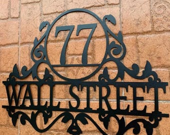 May include: Black metal house number sign with ornate scrollwork and the number 77 and the words "Wall Street" in a decorative font.
