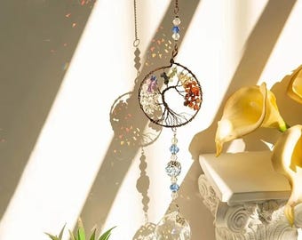 May include: A crystal suncatcher with a wire tree of life design and colorful gemstones. The suncatcher is hanging from a ceiling and has a crystal ball at the bottom.