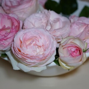 Peut inclure: Un bol en c&eacute;ramique blanche rempli de roses roses. Les roses sont dispos&eacute;es en cercle, les p&eacute;tales se chevauchant.