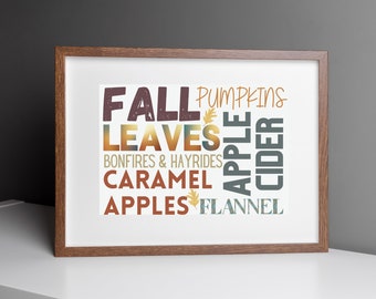 May include: A framed print with a white background and brown frame. The print features a word cloud of fall-themed words in various colors, including "Fall", "Pumpkins", "Leaves", "Bonfires & Hayrides", "Caramel Apples", "Flannel", "Apple Cider".
