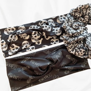 May include: Two black headbands and a scrunchie. One headband features a repeating white skull pattern, while the other has the word "Misfits" in white. The scrunchie also has the white skull pattern.