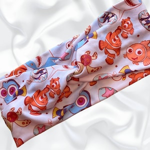 Peut inclure: Un bandeau bleu clair avec un motif répété de poissons, tortues et étoiles de mer en dessin animé. Le bandeau est fait d'un tissu doux et extensible.
