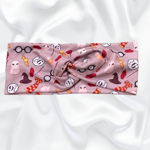 May include: A mauve headband with a repeating pattern of Harry Potter-themed icons. The design includes glasses, owls, feathers, a sorting hat, a scarf, and the number 9 3/4. The headband is twisted at the top.