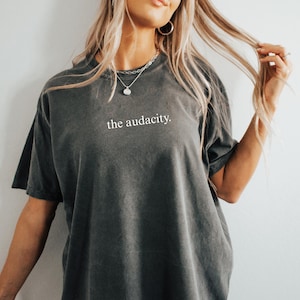 May include: A dark gray oversized t-shirt with the text "the audacity." printed in white on the front.
