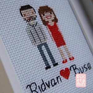 Op de afbeelding: Een kruissteekborduurwerk op witte stof met twee figuren in pixel-artstijl, één in een grijs overhemd en donkere broek, de andere in een rode jurk. Onder de figuren staat de tekst Ridvan, een rood hartje en Buse, met Pixetamin in de hoek.