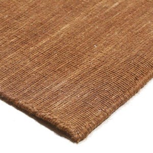 May include: Close-up of a brown woven rug with a textured surface. The rug has a visible weave pattern and a darker brown border. The corner of the rug is visible against a white background.