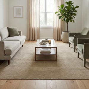 May include: A living room set featuring a light beige sofa with a dark olive green throw pillow, two matching olive green armchairs, and a rectangular glass-top coffee table with a wooden frame, all arranged on a large, textured beige area rug.