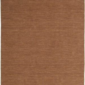 May include: A rectangular, brown rug with a textured surface. The rug has a woven appearance with horizontal lines, creating a subtle pattern. The color is a warm, earthy tone, suitable for home decor.