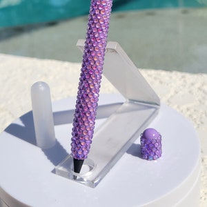 May include: A purple pencil with a clear eraser and a sparkly, iridescent finish. The pencil is standing upright in a clear plastic holder.