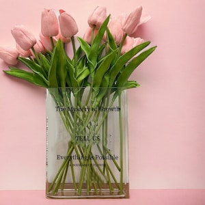 May include: A clear vase with pink tulips and the text "The Mystery of Growth, Tell Us Everything is Possible, A Book About Flower" printed on the side.