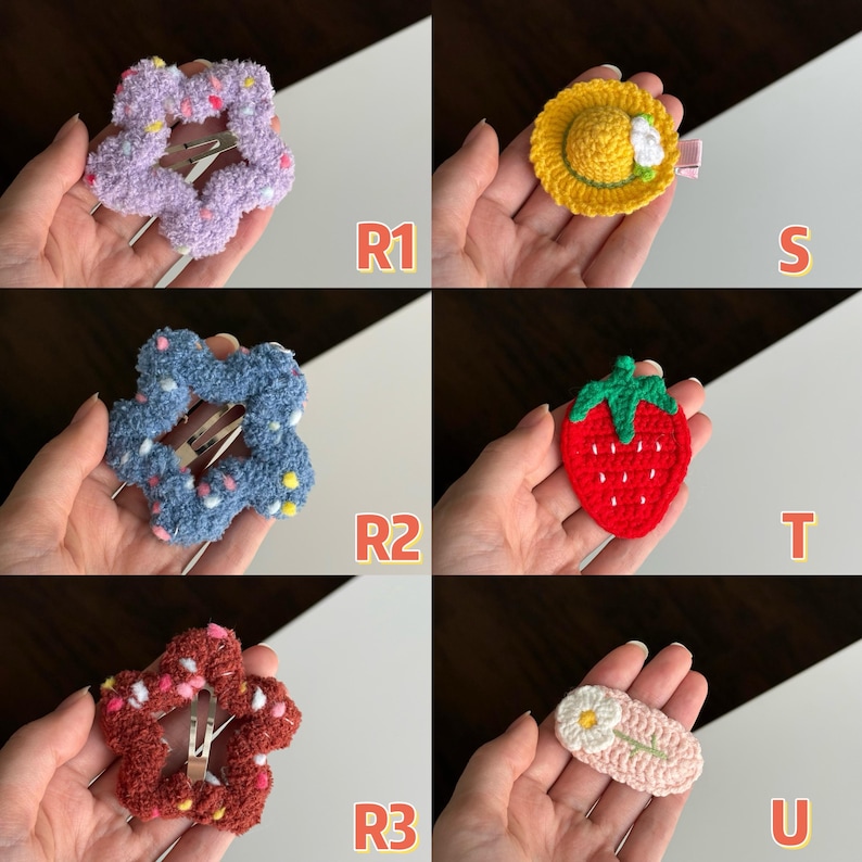 May include: A collection of handmade hair clips in various designs. Includes a lavender flower clip, a yellow crochet hat clip, a blue flower clip, a red strawberry clip, a red flower clip, and a pink daisy clip.