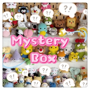 May include: A collection of colorful, crocheted plush toys, including animals and food items, displayed on a wooden pegboard. The text "Mystery Box" is prominently featured. Question mark speech bubbles are scattered throughout the image.