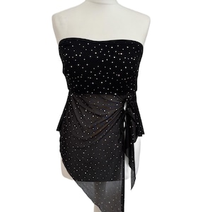 May include: A black strapless top featuring a sweetheart neckline and a sheer, asymmetrical overlay. The entire garment is embellished with small, reflective silver dots. The overlay is gathered at the side with a tie detail, creating a draped effect.