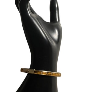 May include: A gold bangle bracelet with a brown and white patterned design.