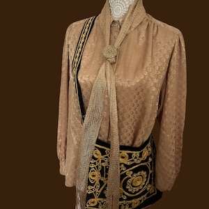 May include: A brown silk blouse with a gold chain and black velvet trim. A gold chain scarf is tied around the neck and a gold chain bag with black embroidery hangs from the shoulder.