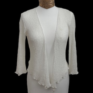 May include: A white ceramic mug with a black handle and the text "But First, Coffee" in a bold, black font. The mug is set against a blurred background, suggesting a cozy setting.