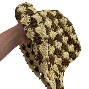 May include: A crocheted hat in a checkerboard pattern of cream and brown. The hat's brim is lined with small wooden beads. The hat is made of a woven material.