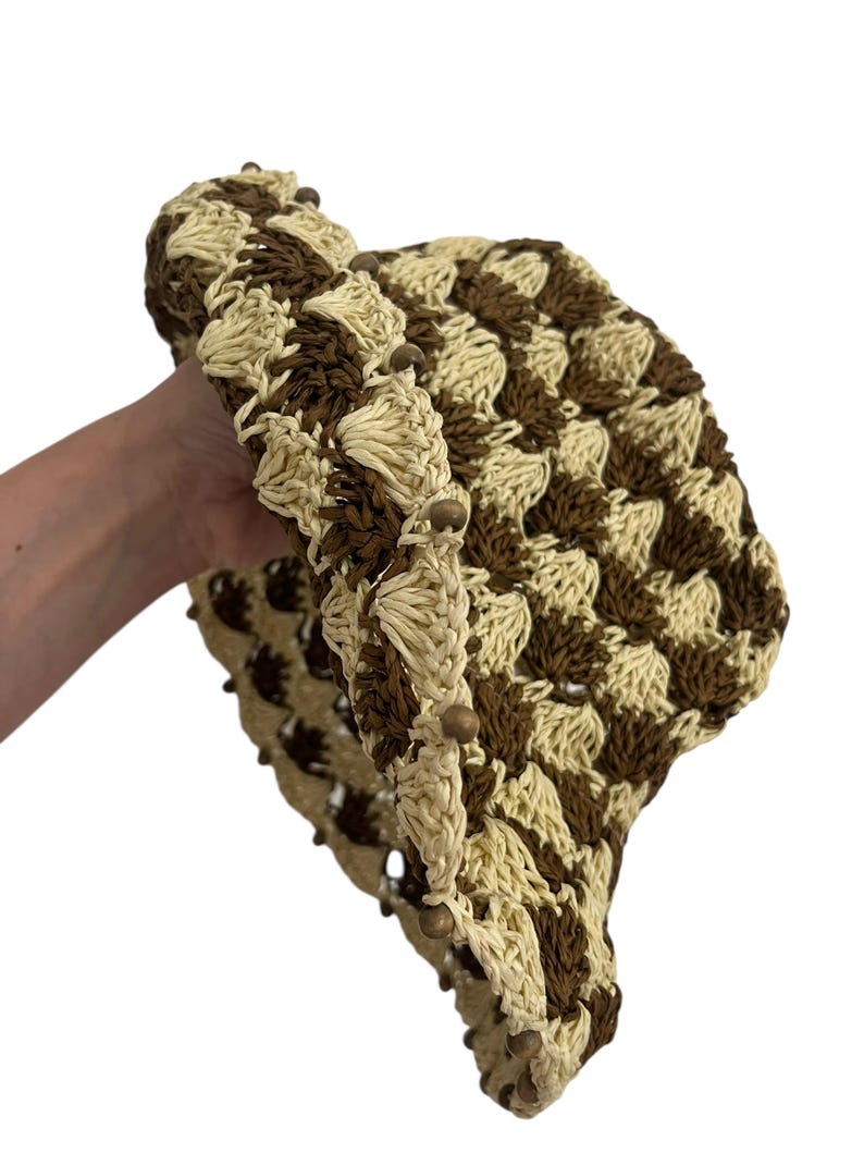 May include: A crocheted hat in a checkerboard pattern of cream and brown. The hat's brim is lined with small wooden beads. The hat is made of a woven material.