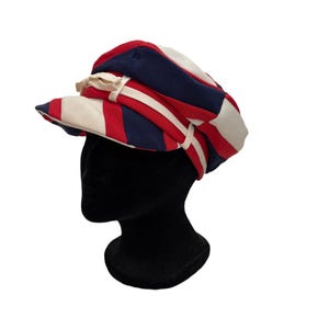 May include: A striped hat in red, white, and navy blue, with a small brim and a decorative bow. The hat is placed on a black mannequin head, showcasing its design and shape. The hat's stripes create a bold, eye-catching pattern.