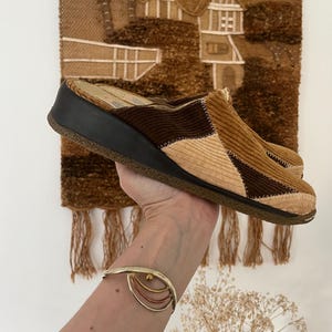 May include: A pair of brown and beige corduroy clogs with a thick black platform sole. The clogs have a patchwork design and are made of a soft, comfortable material.