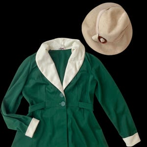 May include: A green blazer with a white collar and cuffs. The blazer has a button closure and a belt. A beige hat with a brown button is also pictured.