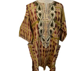 May include: A long-sleeved, brown and green patterned shirt with a V-neck and embroidered details. The shirt has two pockets on the sides.