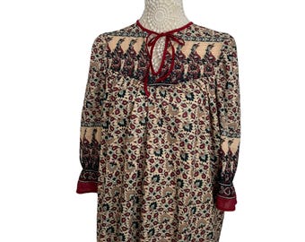 May include: A long-sleeved, cream-colored dress with a red and black paisley print. The dress has a tie at the neckline and a gathered skirt.