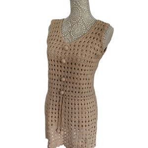 May include: A sleeveless crochet dress in a light brown color. The dress has a V-neckline and a button closure at the front. The dress is made of a delicate crochet fabric with a scalloped hem.