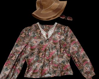 May include: A floral print blouse with a white lace collar and long sleeves. The blouse has a button-up front and a fitted silhouette. A brown hat and sunglasses are also pictured.