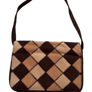 May include: A brown shoulder bag featuring a diamond pattern in shades of brown and beige. The bag has a long strap and a rectangular shape. The diamonds are stitched together, creating a patchwork design. The bag is made of suede.
