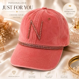 May include: A dusty rose baseball cap with the letter "N" embellished with rhinestones. The cap features a rhinestone band across the brim and the text "PERSONALIZED JUST FOR YOU CHOOSE YOUR INITIAL" in the background. The cap is described as "LUXURY RHINESTONE DETAILS".